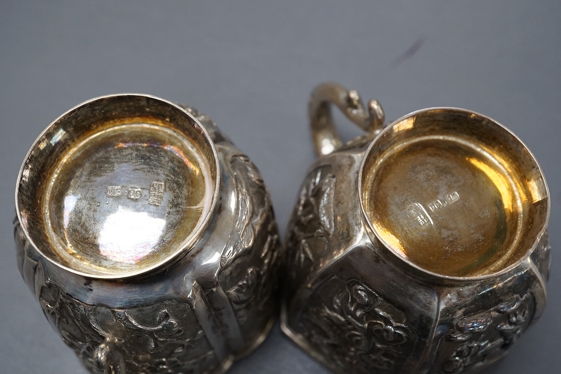Two late 19th/early 20th century Chinese Export white metal tea cups, maker Wing Fat, embossed with bamboo, chrysanthemums and figures, of hexagonal or cusped form, 5.4oz.
